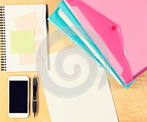 Messy office table with smartphone, notepad and filling folders. View from above