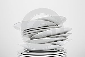 Messy stack of white plates about to fall, isolated on white