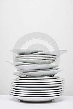 Messy stack of white plates about to fall, isolated on white