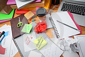 Messy table with laptop and sticky notes, above view. Concept of being overwhelmed by work