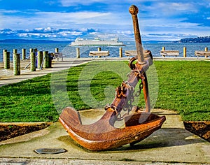 Metal anchor on the beach with a cruise ship on the sea and the clouds in the sky