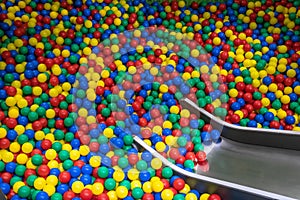 Metal baby slide going down to the pool with many colored balls in the kids playing room