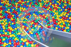 Metal baby slide going down to the pool with many colored balls in the kids playing room