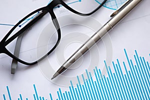 Metal ballpoint pen and glasses for vision lie on documents with graphs in office closeup