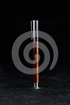 A metal ballpoint pen highlighted on a black background. A pen made of expensive wood, a gift set.