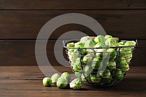 Metal basket with fresh Brussels sprouts on table against wooden background.