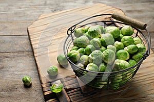 Metal basket with fresh Brussels sprouts on wooden table.