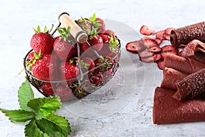 Metal basket with fresh strawberries. Strawberry pastille is rolled up in a tube. Natural product. Dried fruit from strawberries.