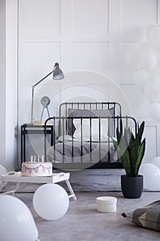 Metal bed with grey bedding and white pillow on the empty white wall, real photo with copy space