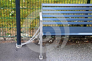 Metal bench on a bus stop, tied to a post with chain, to prevent theft and vandalism