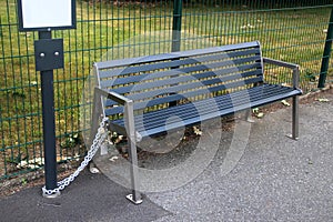 Metal bench on a bus stop, tied to a post with chain, to prevent theft and vandalism