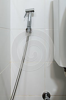 The metal bidet spray is hanging on the white tile wall near the flush toilet