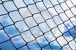 Metal black fence-mesh netting. Blue and white clouds on blue sky. The background image of the fence.