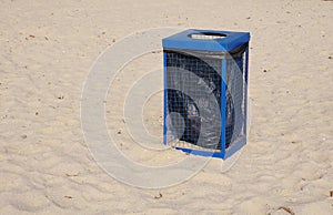 Metal blue garbage dustbin on beach sand