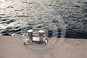 Metal bollard for boats and vessels on wharf over sea and sunset background close up.