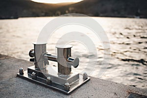 Metal bollard for boats and vessels on wharf over sea and sunset background close up.