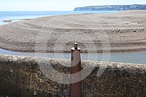 A metal bollard by the breakwater at the mouth of the river Axe near Axmouth in Devon