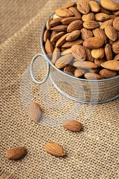 Metal bowl full of almonds on a sackcloth. Pile of nuts stacked together randomly on the burlap background. Healthy nutrition