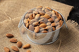 Metal bowl full of almonds on a sackcloth. Pile of nuts stacked together randomly on the burlap background. Healthy nutrition