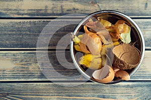 Metal bowl full of organic food scraps and peel rubbish on wooden background. Compost and manure, recycling of waste. E
