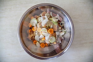 A metal bowl with raw sliced meat, pickled with spices, and vegetables for further cooking.