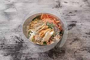 Metal bowl with roasted chicken breast chopped with quinoa, raisins, almonds and grated carrots, parsley and coriander