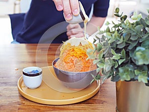 A metal bowl of Thai tea shaved ice topped with egg yolk floss served with condensed milk and Thai glutinous rice balls Bua Loi