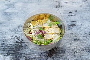 Metal bowl of vegan salad with filleted tofu, sesame seeds, assorted lettuce, sweet corn, sunflower seeds,