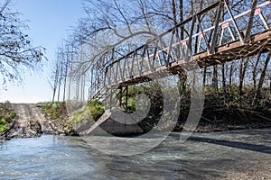 Metal bridge over a fast-flowing river with leafless poplars