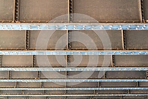 Metal bridge with steel girders on bottom or underneath with rivets and metal bars and beams for shady industrial design