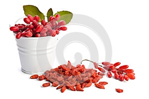 Metal bucket with berberries near heap of goji berries