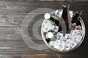 Metal bucket with bottles of beer and ice cubes on wooden background, top view. Space for text