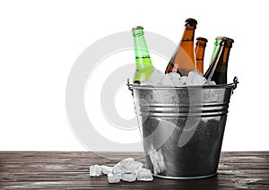Metal bucket with bottles of beer and ice cubes on table against white background. Space for text