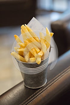 Metal bucket is filled with French fries costs on a chair back