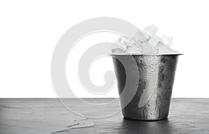 Metal bucket with ice cubes on table against background