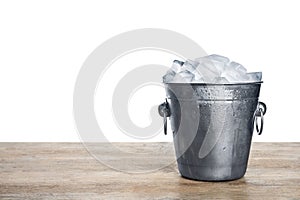 Metal bucket with ice cubes on table against white background