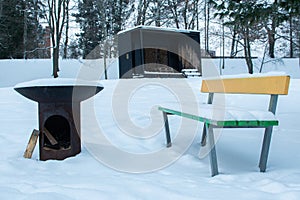 Metal campfire and colorful wooden bench covered in snow in a park in Finland