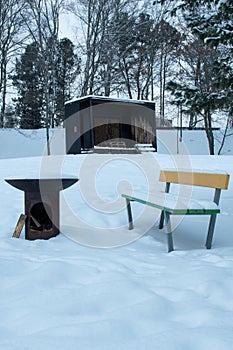 Metal campfire and colorful wooden bench covered in snow in a park in Finland