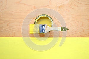 Metal can yellow paint, brush with natural bristles, wooden handle on plywood