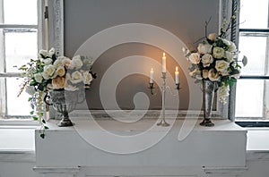 Metal candle holder with burning candles and vases with artificial flowers on a pedestal