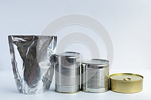 Metal cans of different sizes, metallized flexible packet on a white background. A variety of packaging for canned food.