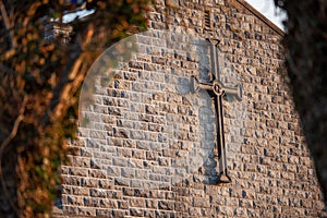 Metal catholic cross on a stone wall, framed by dark trees branches out of focus. Concept catholic faith symbol and religion