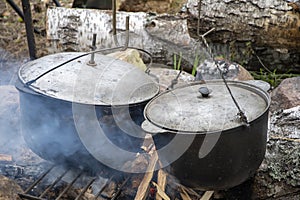 Metal cauldrons with lids are heated and smoked on a fire in the forest, tourist dishes for cooking.