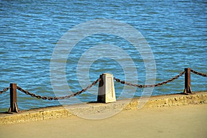 Metal chain railing with cement posts on side of ocean at fisherman\'s warf or near harbor in downtown city near waterfront