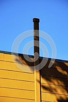 Metal chimney vent or pipe on building or home exterior with orange horizontally slatted or panneled facade with blue