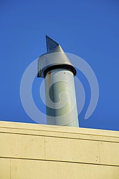 Metal chimney vent or pipe with gray metal in shade with wooden slat foreground beige color and blue and dark sky