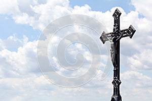 Metal christian cross on blue cloudy sky background, copy space. Catholic church symbol, Jesus Christ Faith, spirituality