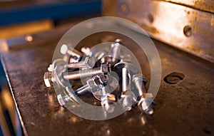 Metal chrome bolts and nuts lie on the shiny metal surface of the machine