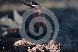 Metal clamp grabbing chinchulines and molleja, cooked on the coals in a grill.