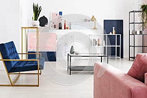 Coffee table with glass counter top in the middle of modern full of color living room with petrol blue armchair, powder pink